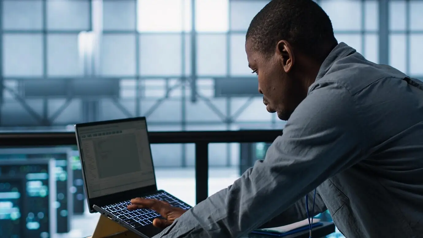 Техник в центре обработки данных работает на ноутбуке, используя языки программирования.